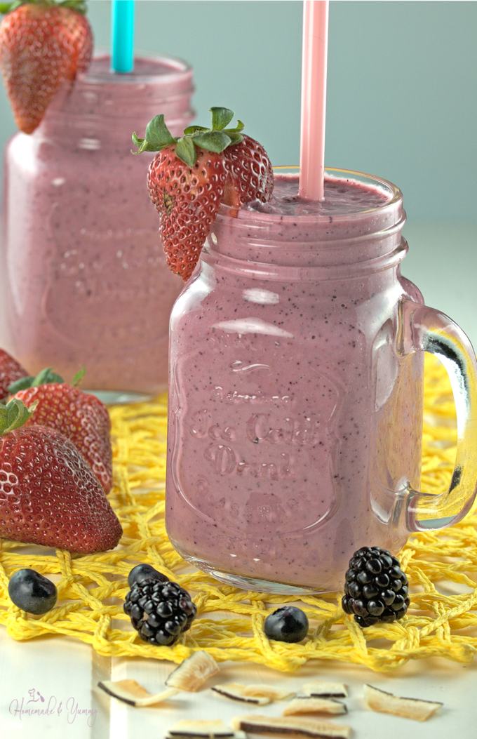 Two smoothies with straws and garnished with berries.