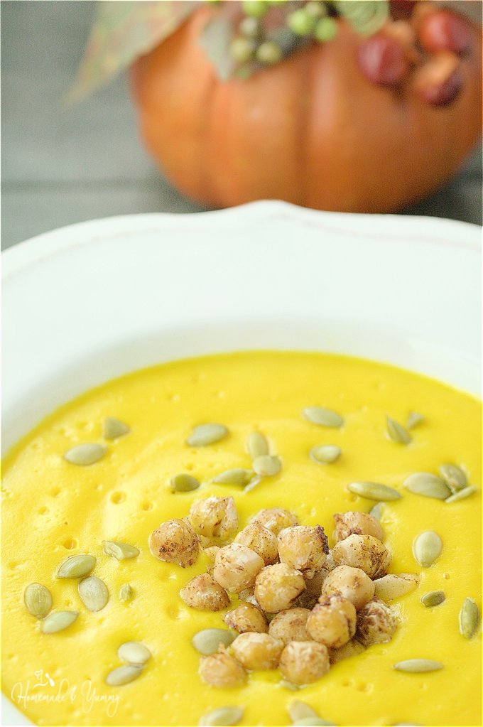 Close up overhead shot of pumpkin soup in a bowl, garnished with chickpeas.