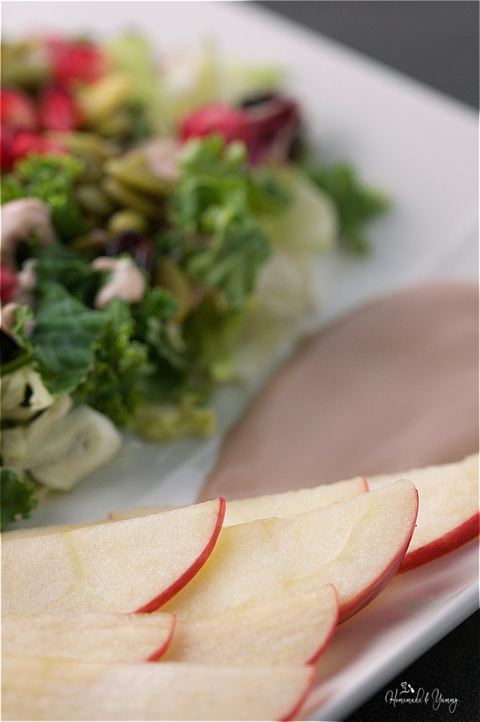 Close up shot of sliced apples on a plate, some salad in the background.