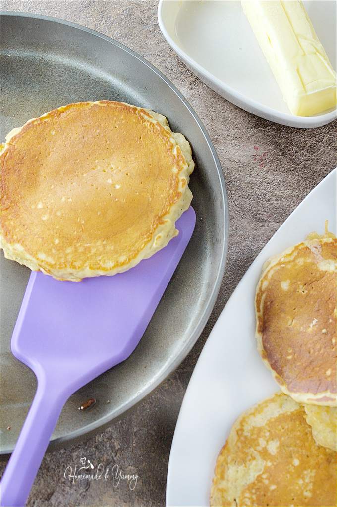 Pancakes in the frying pan, and some on a plate on the side.