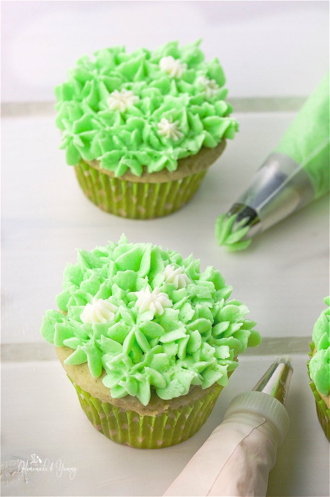Close up of the Green Tea cupcakes getting decorated with green icing, piping bag in the background.