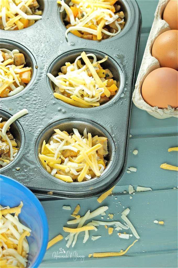 Close up shot of the muffin tin filled with the recipe mixture, topped with shredded cheese ready to go into the oven.