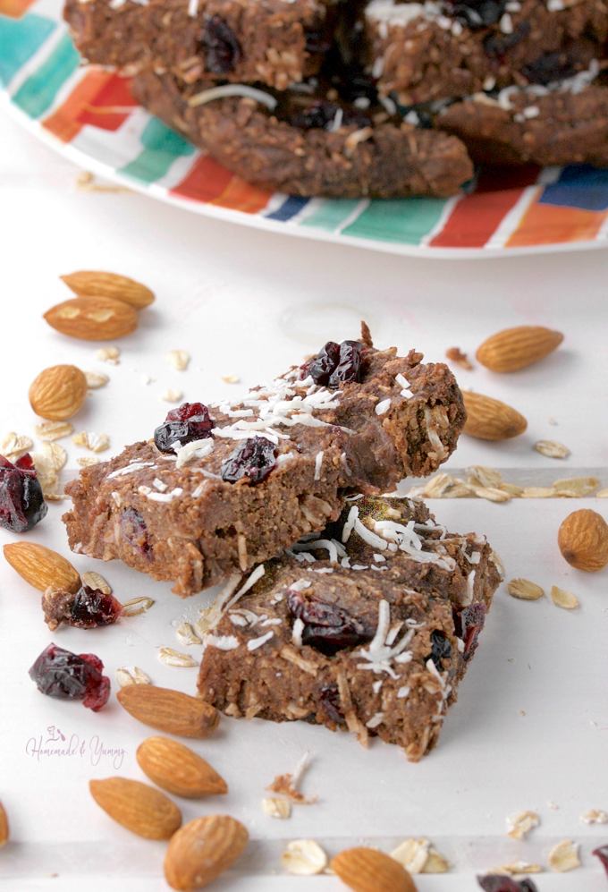 2 pieces of the chewy granola bars with almonds and cranberries sprinkled around, more bars on a plate in the background.