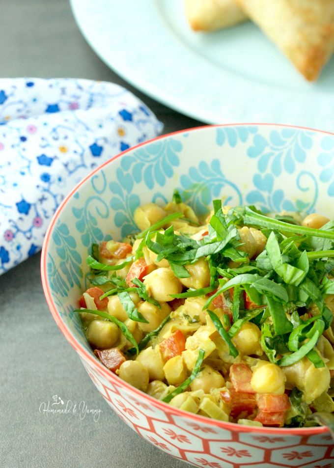 Patterned white and blue bowl with curried chickpeas, diced red peppers and slivered basil in it.