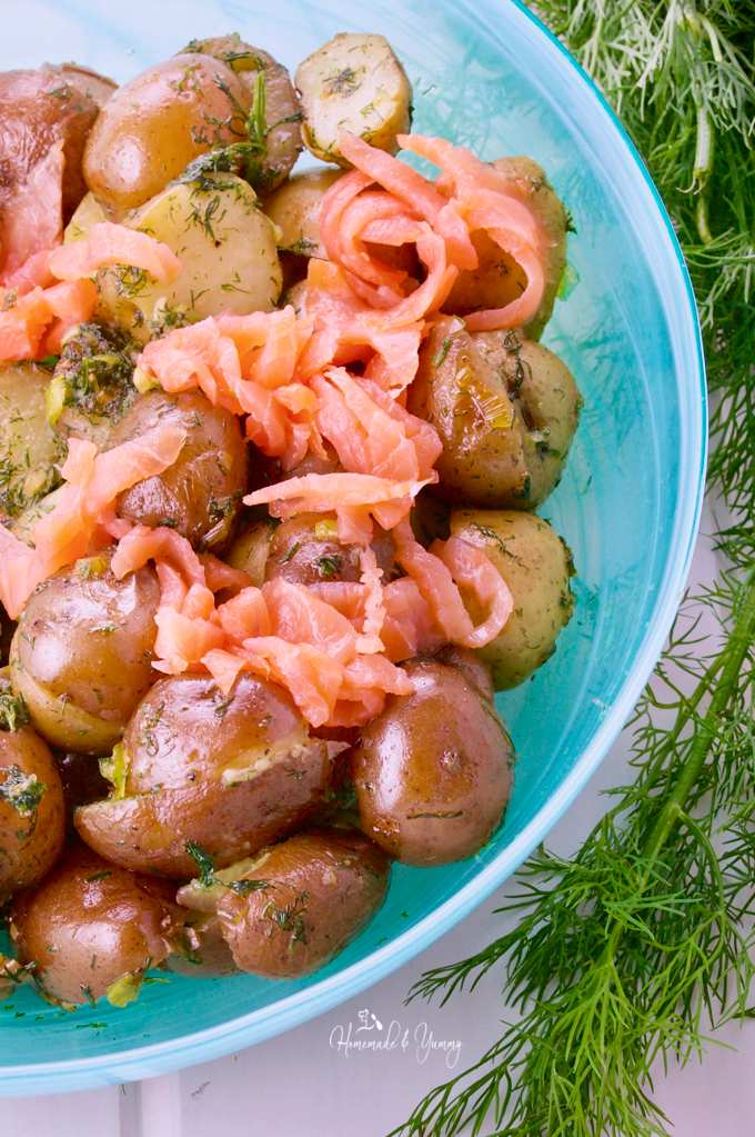Close up shot of cooked baby potatoes and thinly sliced smoked salmon in a bowl with dill sauce.