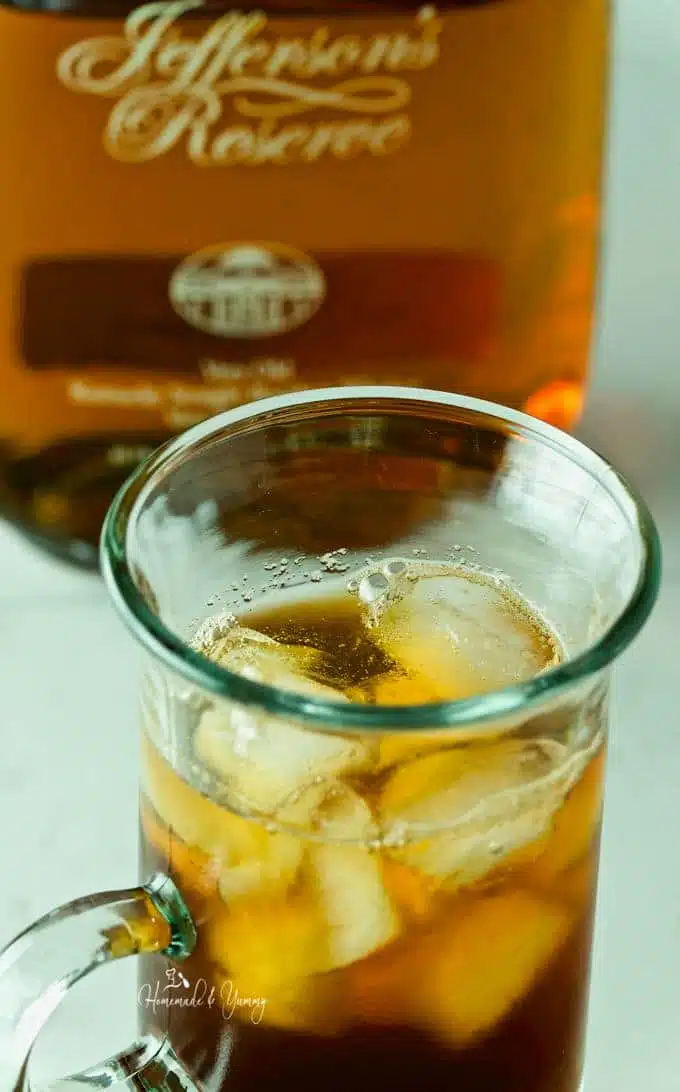 Close up of coffee and ice in a glass with bourbon bottle in the background.