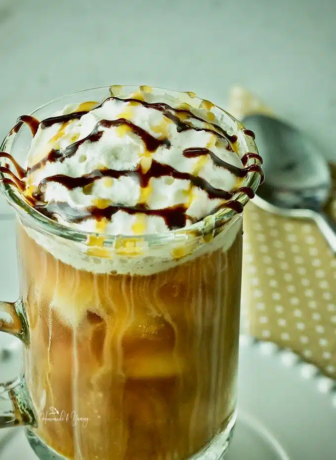 Close up shot of iced coffee in a glass mug with whipped cream and drizzled with chocolate and caramel sauce.