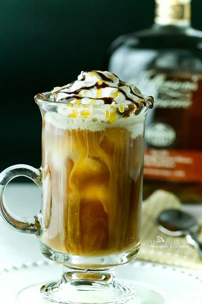 Iced coffee in a glass with whipped cream and drizzle topping. Bourbon bottle in the background.