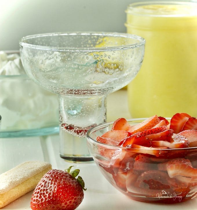 An empty serving dish with sliced strawberries, lemon curd and whipped cream in the background.