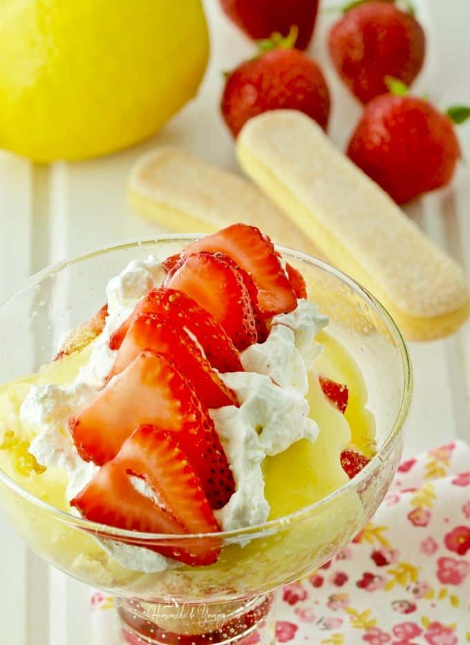 Lemon curd in a bowl topped with whipped cream and sliced fresh strawberries.