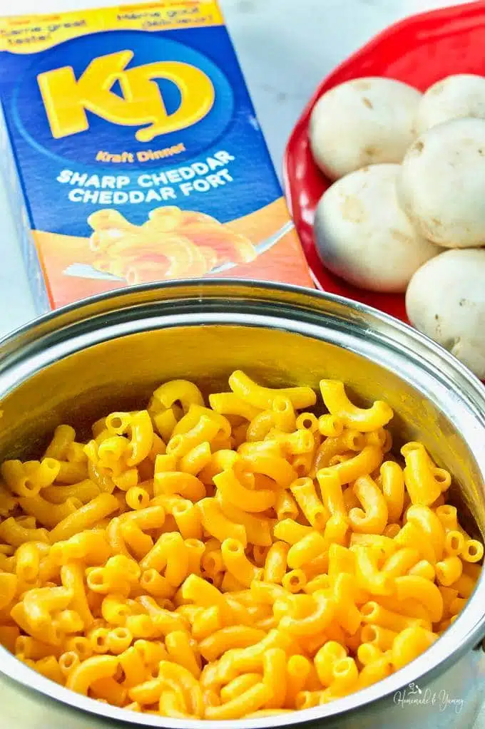 Kraft dinner in a pot with the package and mushrooms in the background.