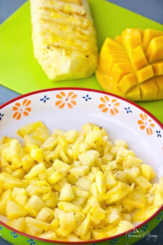 Close up shot of pineapple diced up in a bowl with mango in the background.