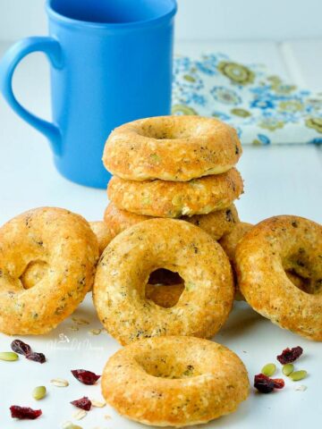 A pile of Oatmeal Breakfast donuts piled on the table with a blue coffee mug in the background.