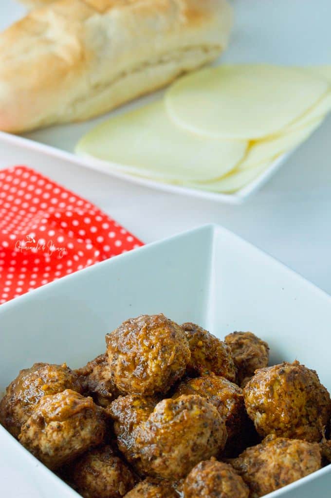 Meatballs in a serving bowl, bread and cheese in the background.