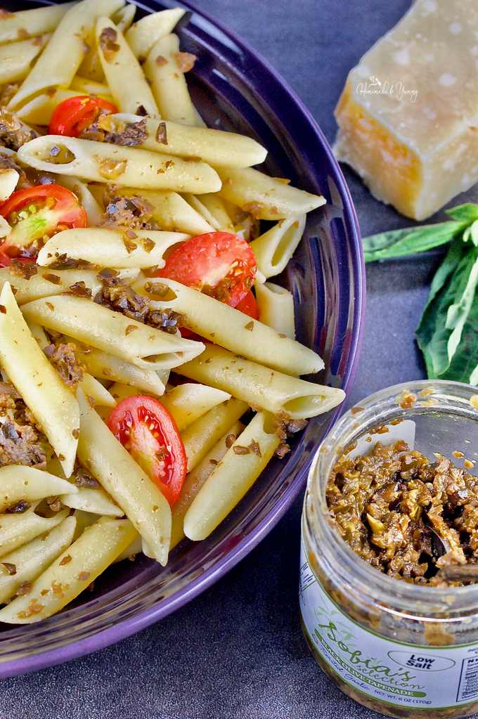 A bowl of penne past in a large bowl and the olive tapenade on the side ready to mix in.