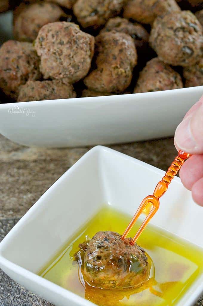 Meatball getting dipped in a bowl of olive oil just before eating.