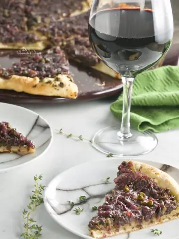 A piece of Pissaladiere French Pizza on a serving plate with a glass of wine.