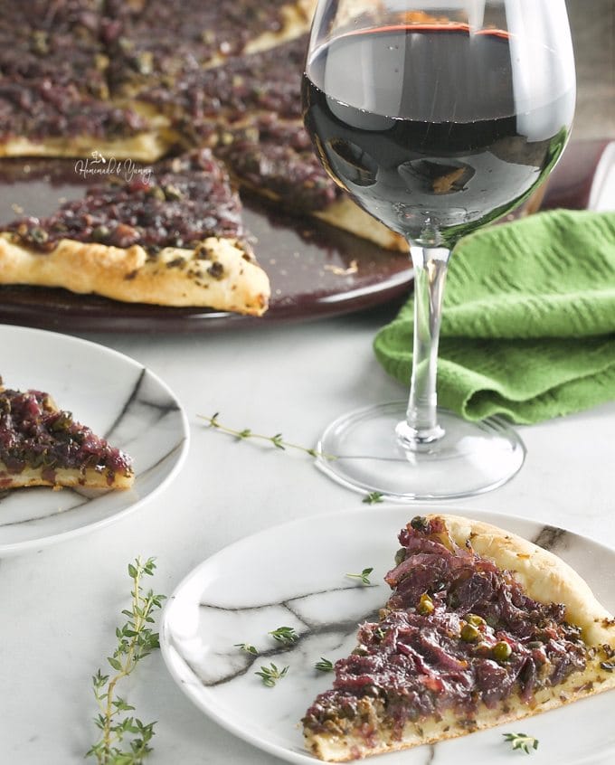  A slice of Pissaladiere French Pizza on a plate and a glass of wine.