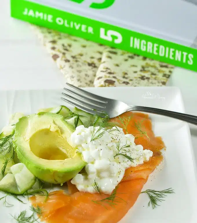 A plate with smoked salmon slices, cottage cheese, avocado, cucumber and dill.