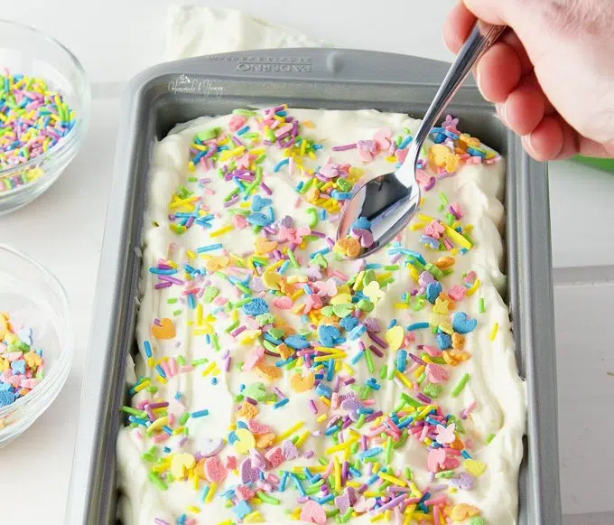 Homemade no-churn ice cream in a pan getting topped with sprinkles.