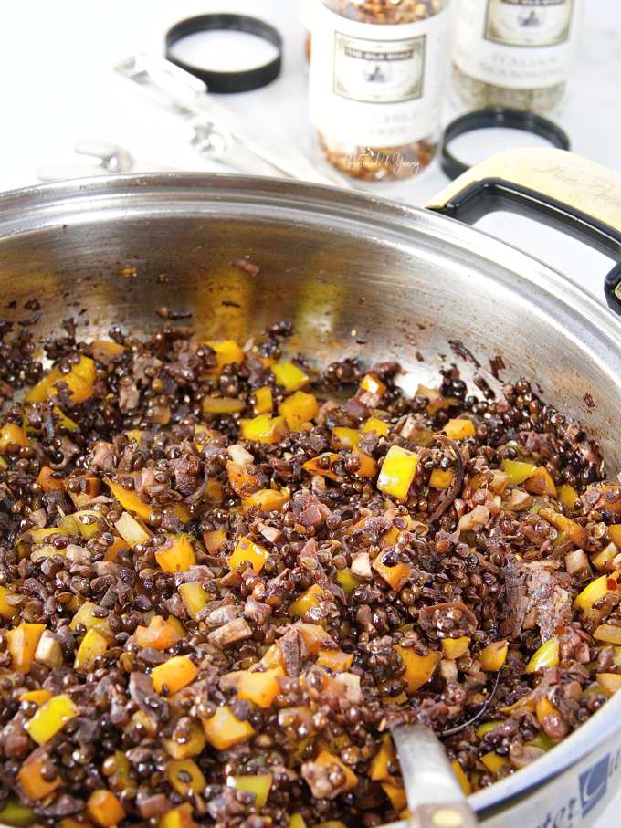 Black lentils cooking in a pan with peppers and mushrooms.