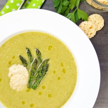 Overhead shot of Asparagus Soup with Wine & Cheese in a bowl garnished with cheese crips and asparagus tips.