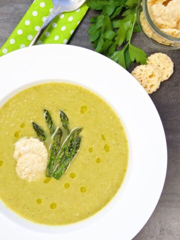 Overhead shot of Asparagus Soup with Wine & Cheese in a bowl garnished with cheese crips and asparagus tips.