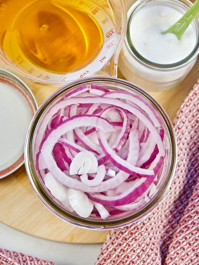 Sliced onions in a jar and pickling ingredients to add to the jar.