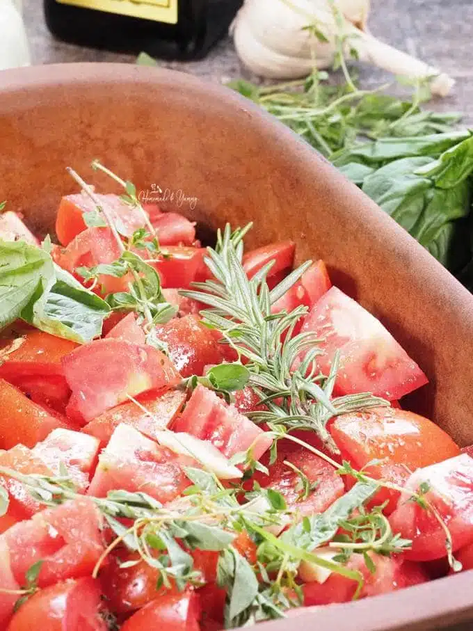 Tomatoes cut up in a baking dish, with oil, spices and herbs.