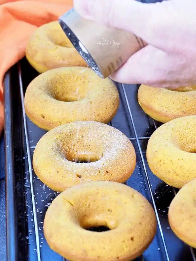 Baked donuts getting topped with cinnamon sugar.