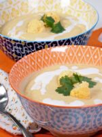 Close up of Roasted Orange Cauliflower Blender Soup with Curry in a bowl garnished with coconut milk and raw cauliflower florets.