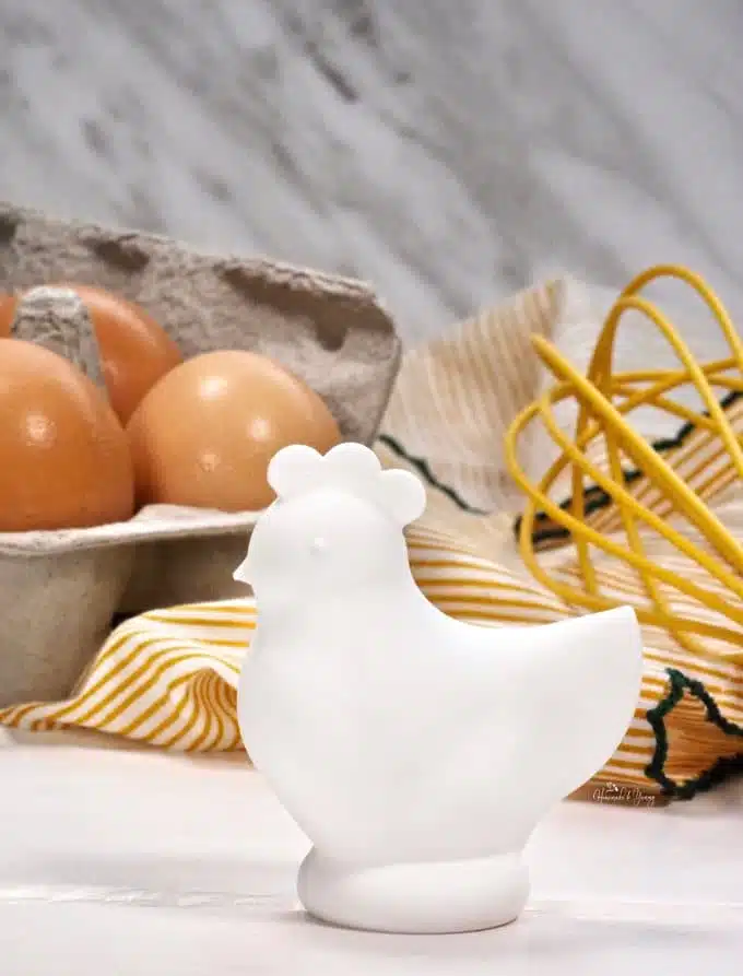 A mini chicken statue with a carton of eggs in the background.