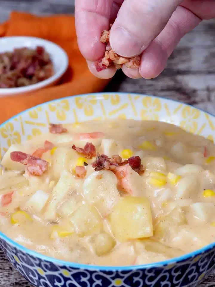 Bacon bits getting added to a bowl of creamy fish and potato soup.