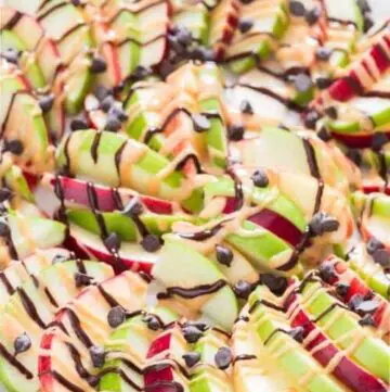 A plate of sliced apples drizzled with peanut butter and chocolate chips.