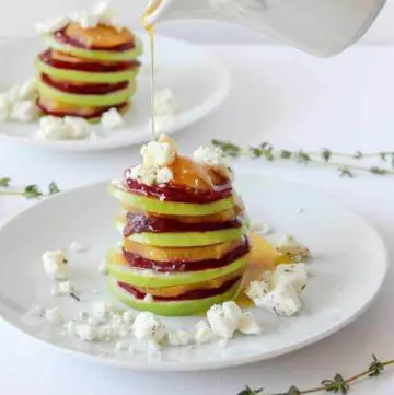 Salad of sliced apples and beets stacked on a plate.