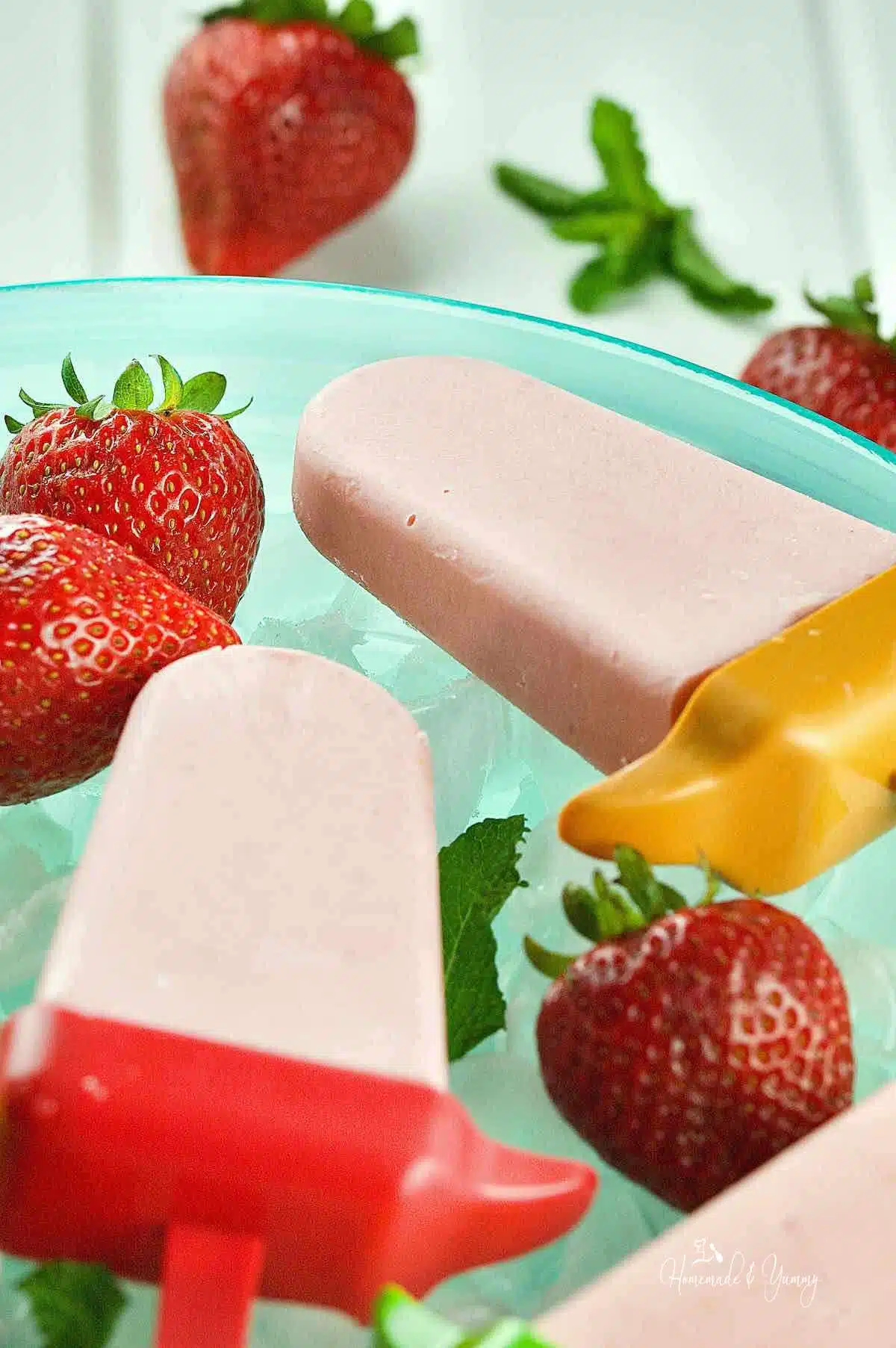 Creamy strawberry cheesecake popsicles on a bed of ice in a bowl.