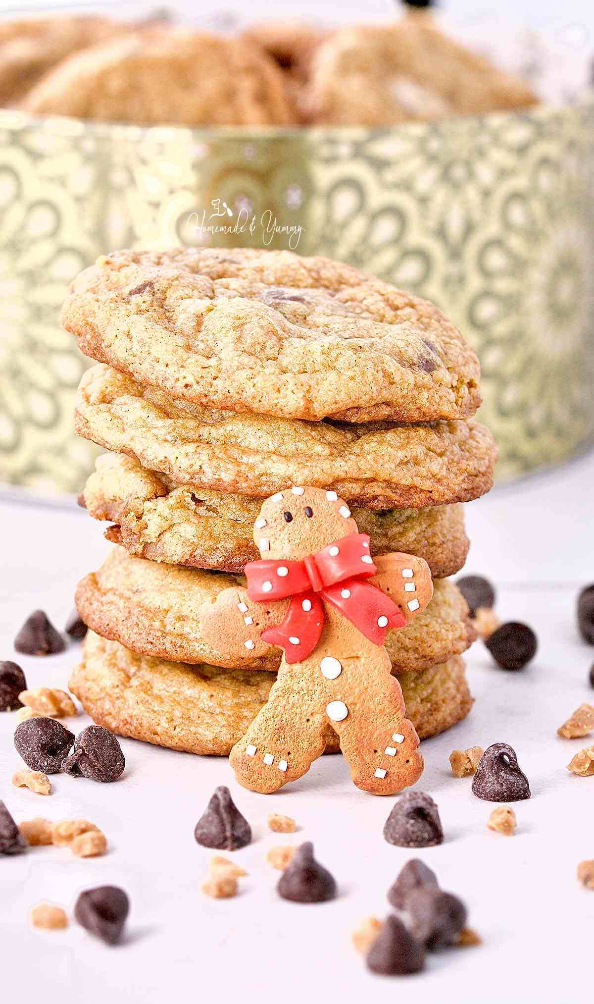 A pile of Gingerbread Chocolate Chip Cookies in front of a holiday cookie tin.