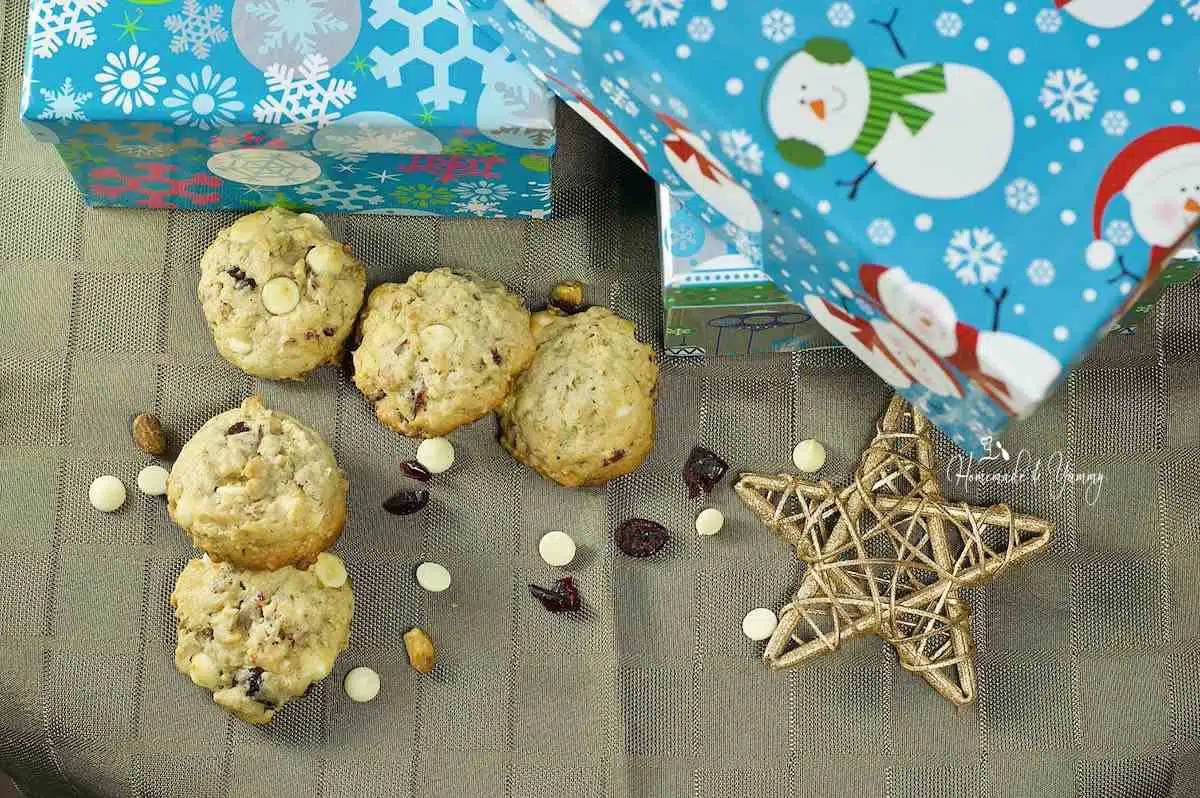 A pile of cranberry oatmeal cookies and Christmas presents on a table.