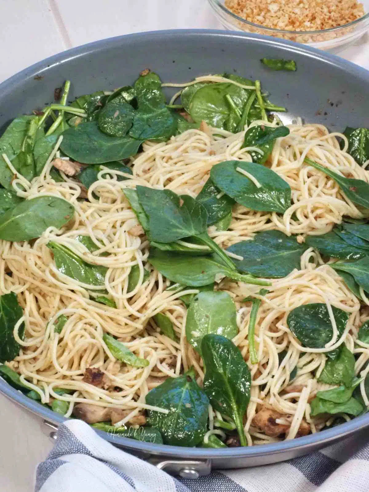 Spaghetti with sardines, mushrooms and spinach in a pan.