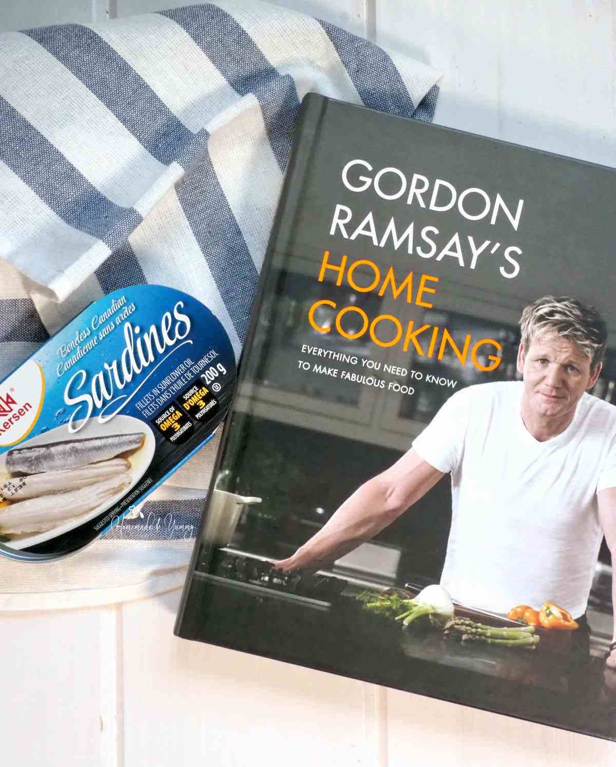 A can of sardines alongside a Gordon Ramsay cookbook.