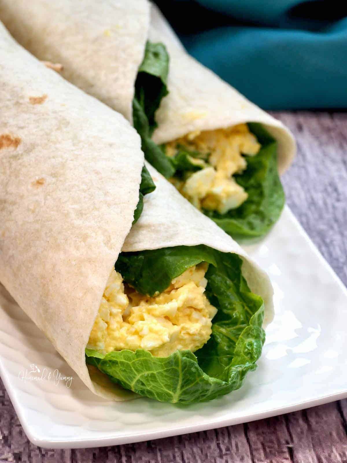 Two Egg Salad Wraps on a white plate.