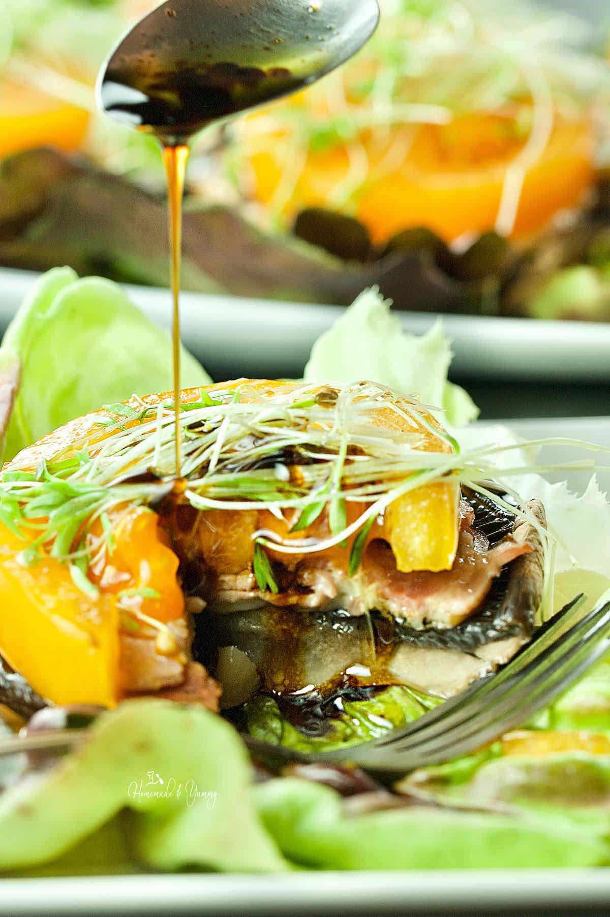 Grilled mushroom stack getting drizzled with dressing.