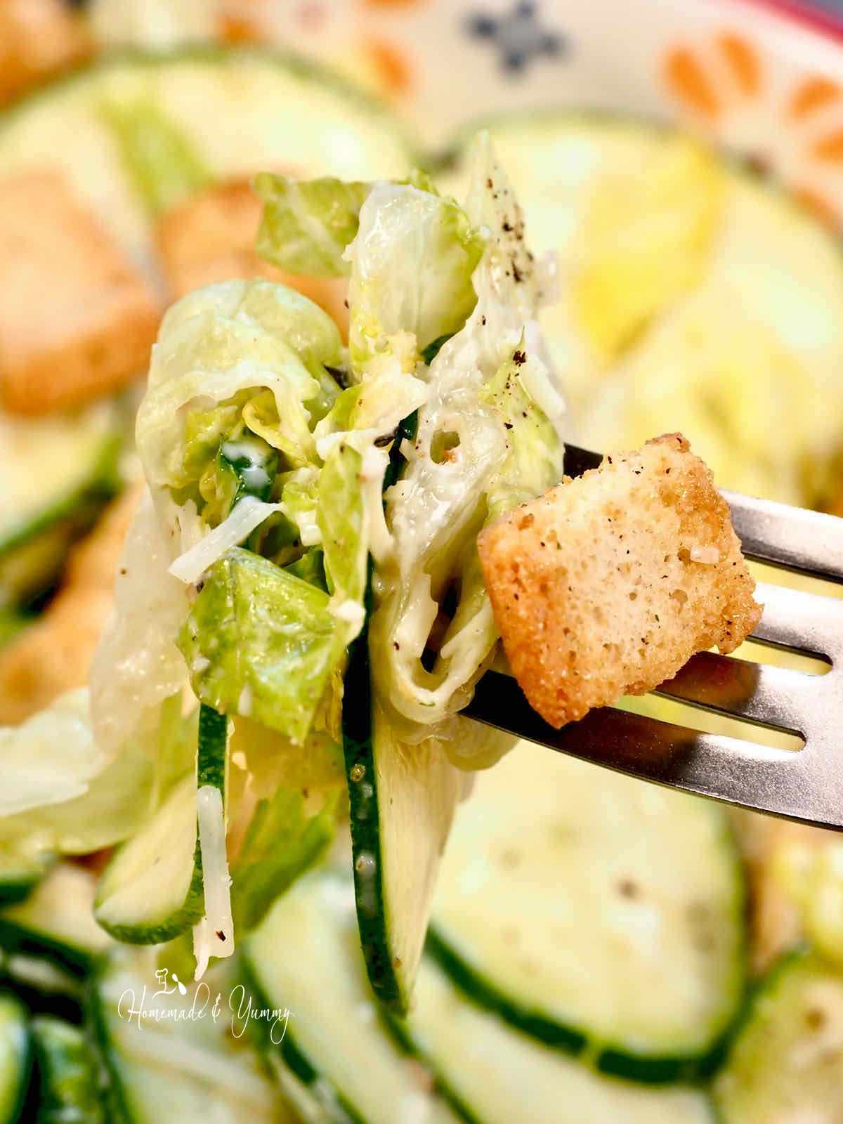 A fork full of caesar salad made with raw zucchini.