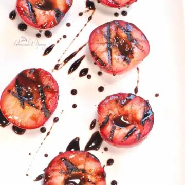 Grilled red plums on a plate with a chocolate honey glaze.