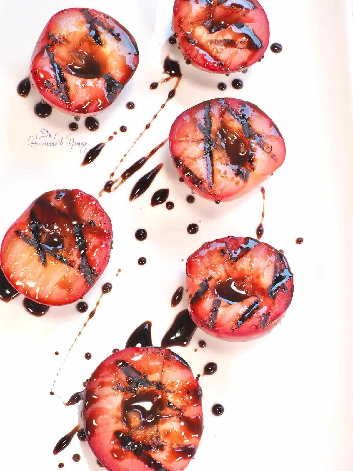 Grilled red plums on a plate with a chocolate honey glaze.