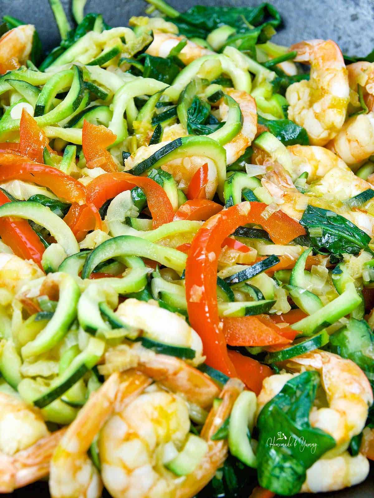 Zucchini zoodles, shrimp, and red peppers cooking in a skillet.