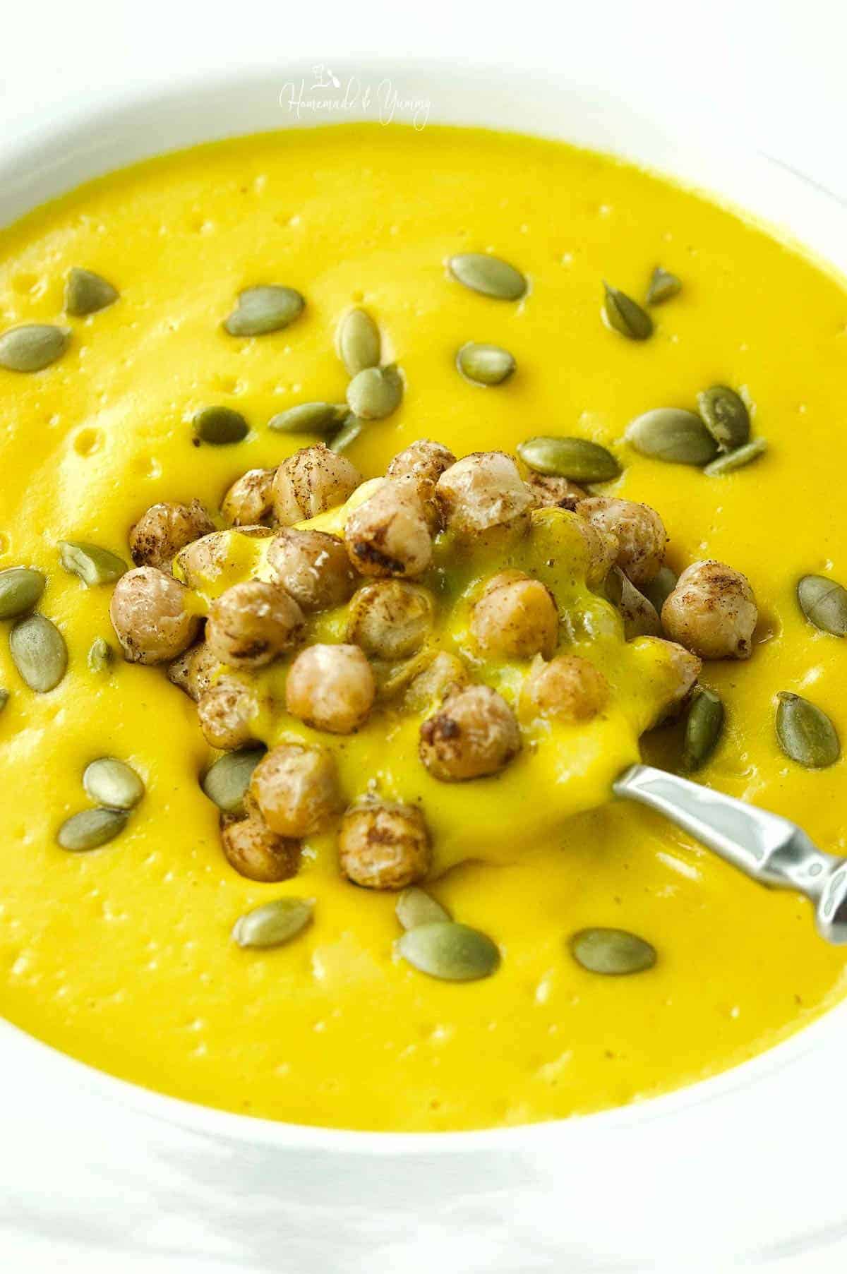 A spoonful of creamy pumpkin soup with roasted chickpea garnish.