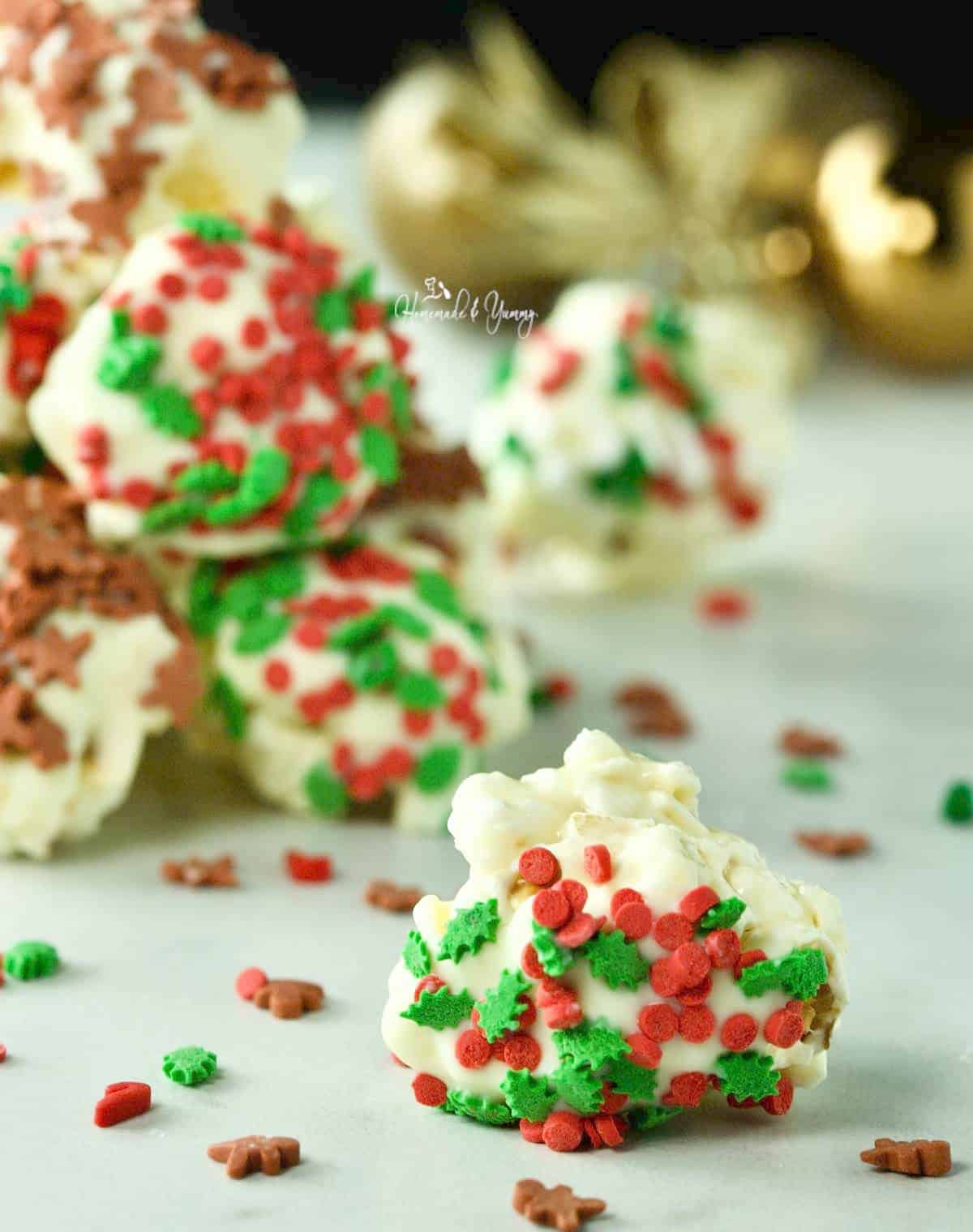 Mini holiday popcorn ball with white chocolate and festive sprinkles.
