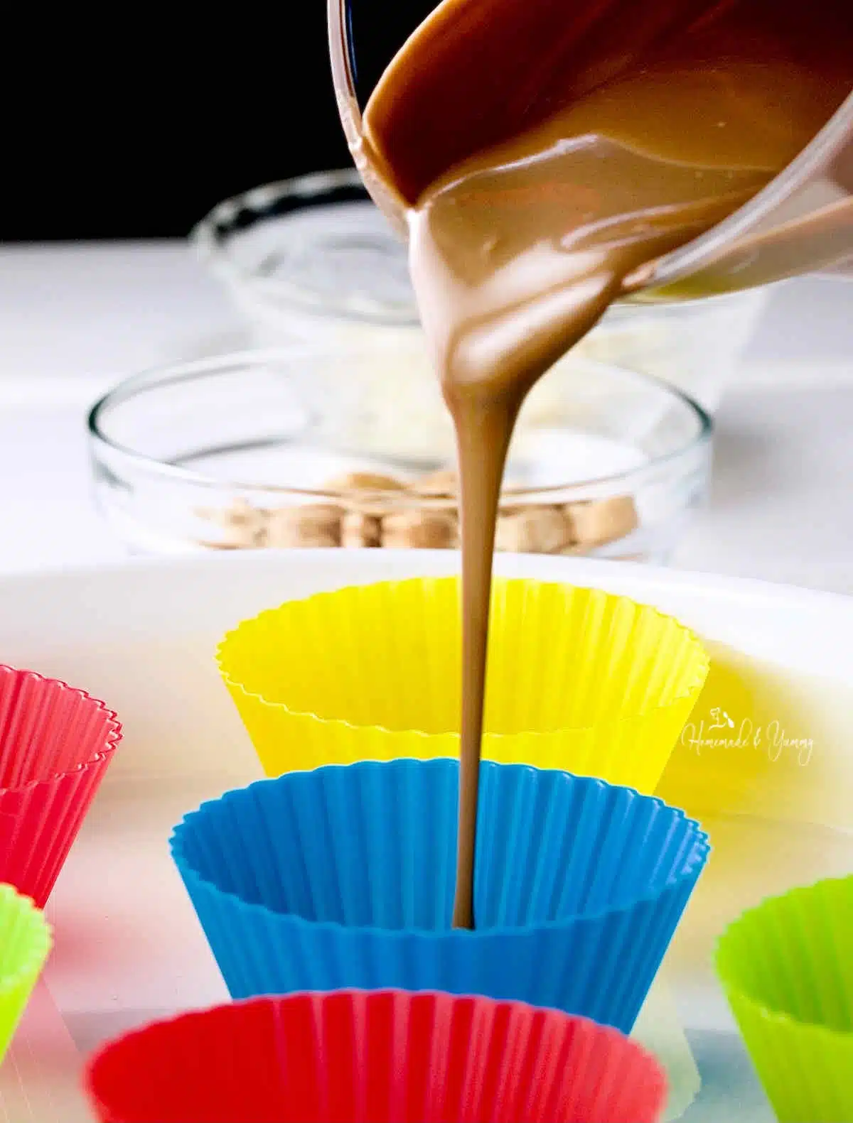 Pouring melted chocolate and peanut butter into silicone cups.
