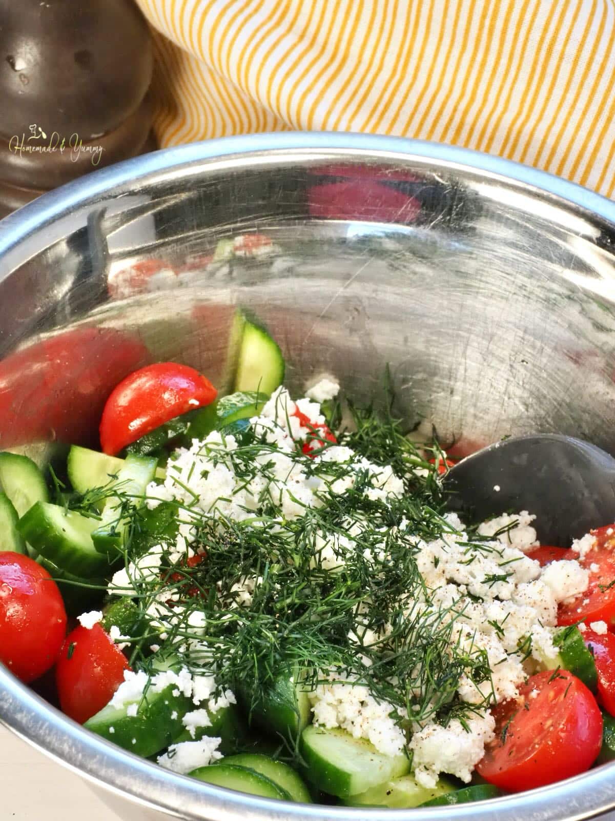 Adding the feta cheese and dill to the cucumber salad.